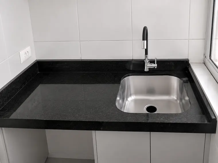 Bancada de granito preto com cuba inox embutida e marcenaria clara